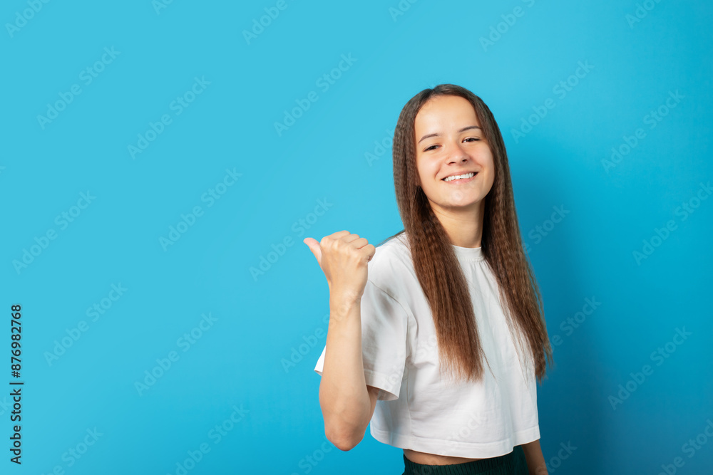 Teenager portrait on green background, points to an empty space for text, copy space, young cute emotional student, attractive female smiling, happy student with curly hair, youthful and positive