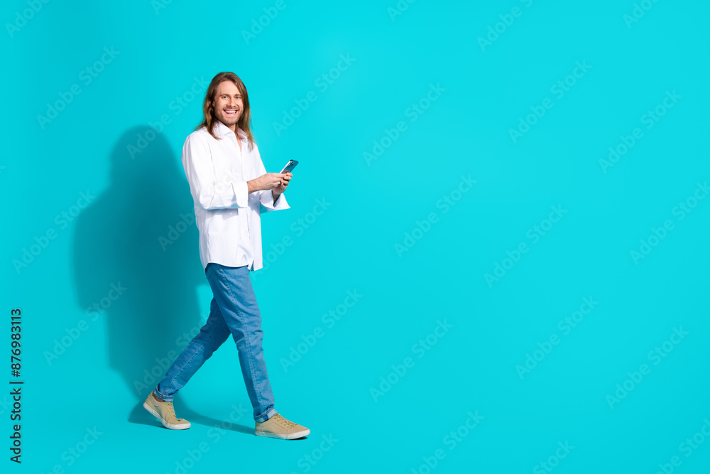 Full length photo of funky cool guy dressed white shirt typing modern device walking emtpy space isolated teal color background Full length photo of funky cool guy dressed white shirt typing modern device walking emtpy space isolated teal color background