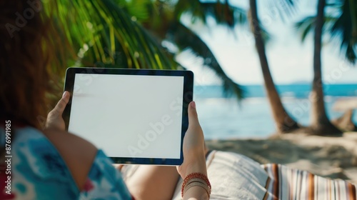 Mockup image of a woman using tablet with blank white desktop screen while sitting on a beach. The concept of freelancing and vacationing. The concept of workaholism