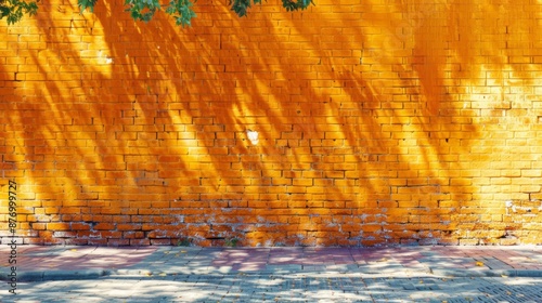 A bright yellow brick wall is contrasted by the dappled shadow of tree branches, creating a striking urban scene that blends natural and human-made textures artistically. photo