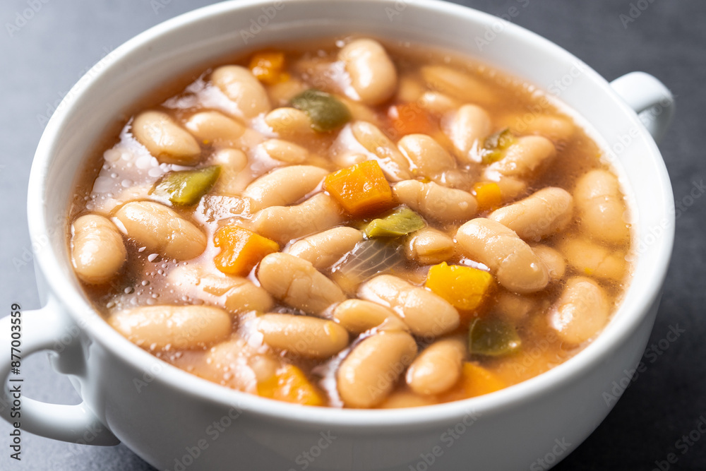 White beans soup with vegetables in white bowl on black stone. Close up White beans soup with vegetables in white bowl on black stone. Close up