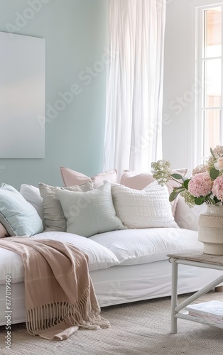 A white sofa with soft pastel throw pillows and a blanket, in a bright living room.