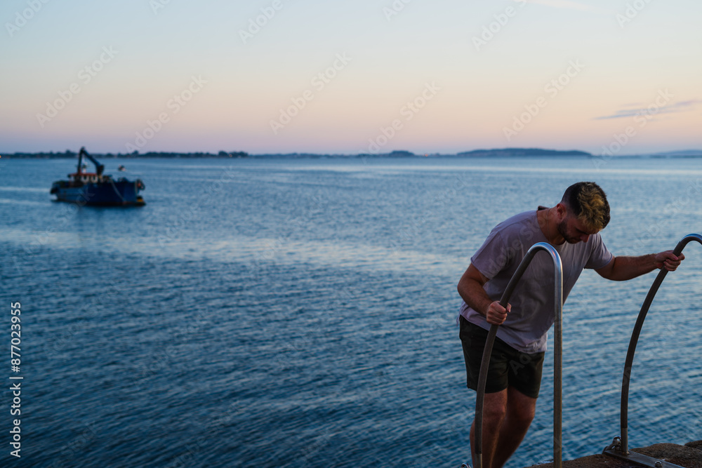 Fototapeta premium Man climbing stairs. back view on the sea shore. In the background the port, boat, pier.