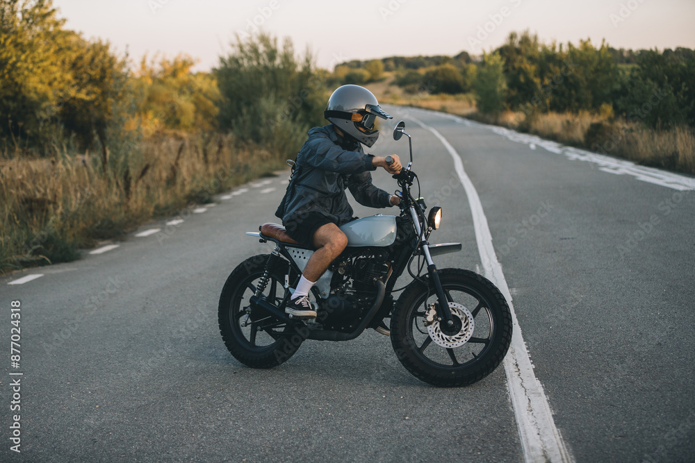 A young man in a helmet and goggles is enjoying his motorcycle on the road at sunset A young man in a helmet and goggles is enjoying his motorcycle on the road at sunset