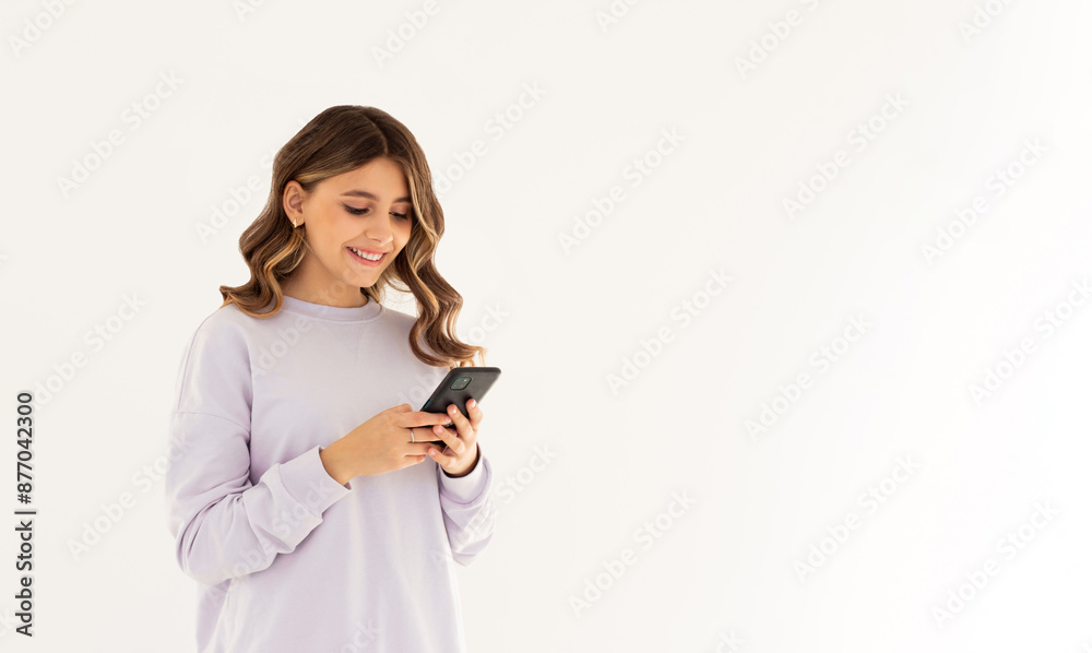 Happy pretty young woman model holding smartphone looking at cell texting message, smiling girl using mobile apps on cell phone standing isolated on white background with cellphone. Happy pretty young woman model holding smartphone looking at cell texting message, smiling girl using mobile apps on cell phone standing isolated on white background with cellphone.