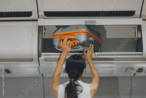 Young Female Tourist Storing Luggage in Overhead Compartment on Airplane During Travel photo