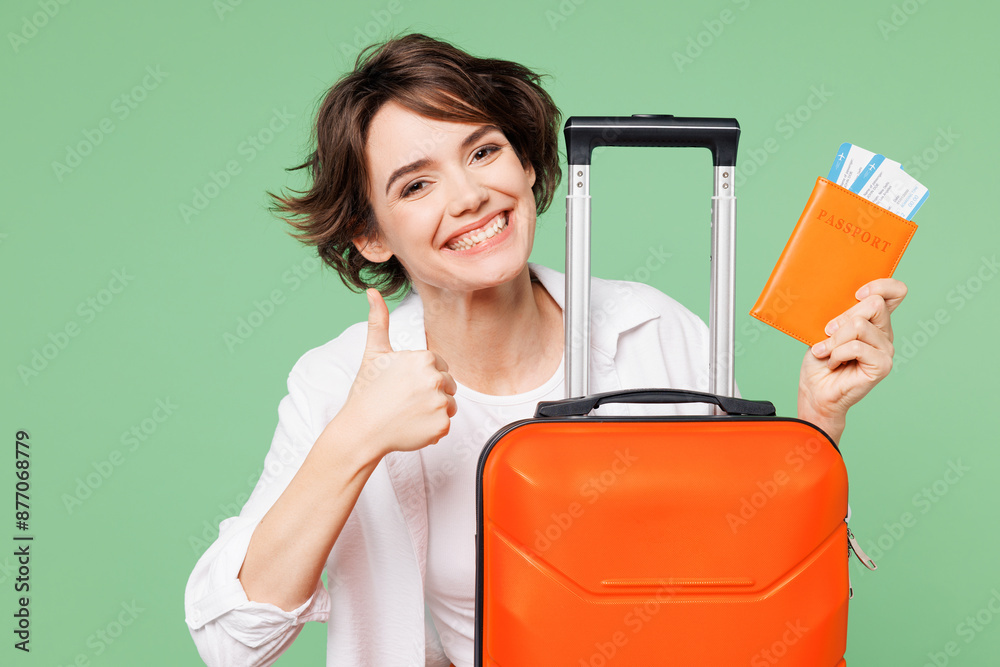 Close up traveler woman wear casual clothes hold passport ticket bag show thumb up isolated on plain green background. Tourist travel abroad in free spare time rest getaway. Air flight trip concept. Close up traveler woman wear casual clothes hold passport ticket bag show thumb up isolated on plain green background. Tourist travel abroad in free spare time rest getaway. Air flight trip concept.