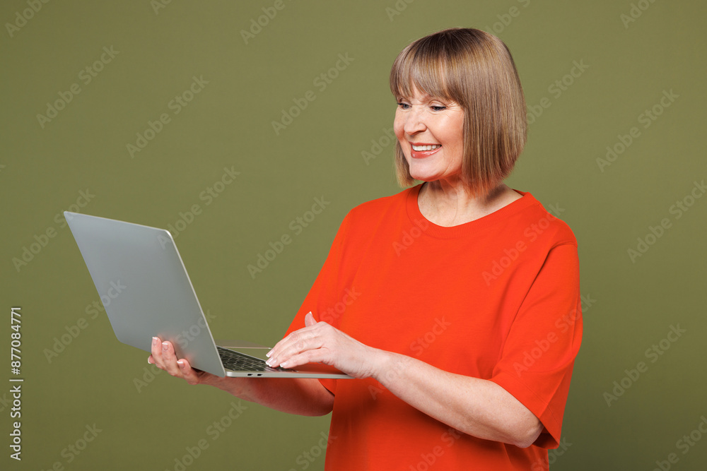 Φωτογραφία Elderly blonde IT woman 50s years old she wear orange t-shirt casual clothes hold use work on laptop pc computer surfing internet isolated on plain pastel green background studio