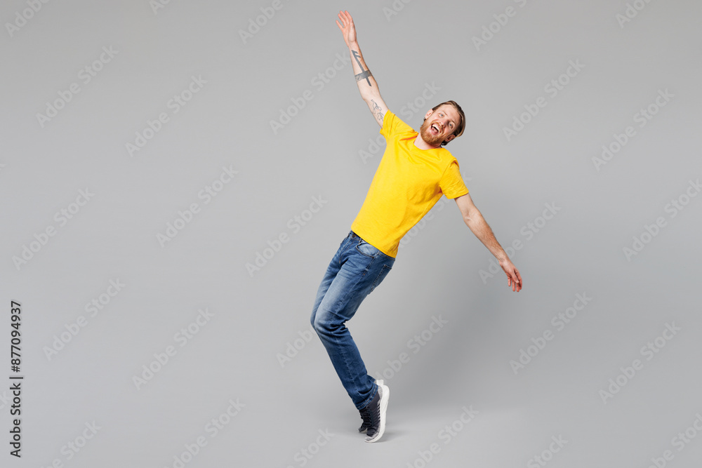 Fototapeta premium Full body young happy cheerful fun man he wear yellow t-shirt casual clothes stand on toes with outstretched hands lean back dance isolated on plain grey background studio portrait. Lifestyle concept.