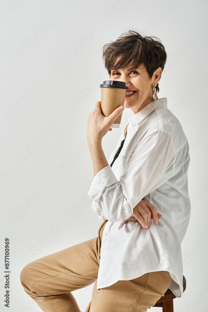 A stylish middle-aged woman with short hair sits on a chair, peacefully holding a cup of coffee. A stylish middle-aged woman with short hair sits on a chair, peacefully holding a cup of coffee.