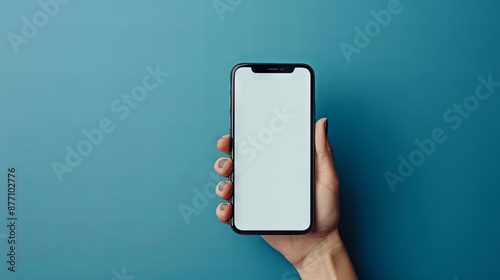In a blue studio background a hand holds a phone with a blank screen promoting an app The mockup offers a wide view and copy space