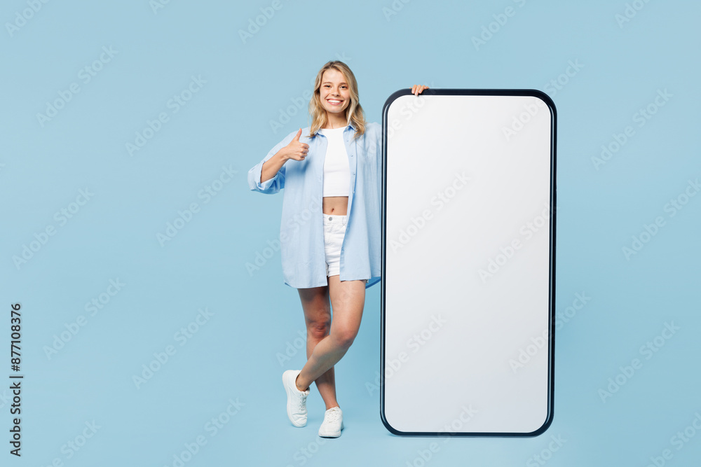 Full body young happy woman wearing white top shirt casual clothes big huge blank screen mobile cell phone smartphone with area isolated on plain pastel light blue cyan background. Lifestyle concept. Full body young happy woman wearing white top shirt casual clothes big huge blank screen mobile cell phone smartphone with area isolated on plain pastel light blue cyan background. Lifestyle concept.