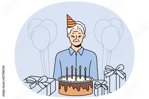 Sad old birthday person celebrating alone standing near table with gifts and cake and needing support of friends. Frustrated grandfather is sad because there are no guests for birthday parties
