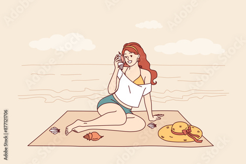 Woman sits on beach and listens to sound of sea from shell, enjoying summer vacation at tropical resort. Tourist girl sunbathes on beach of paradise island in ocean during weekend.