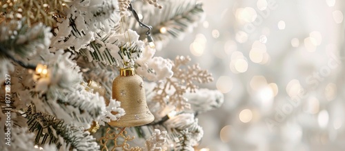Fototapeta Naklejka Na Ścianę i Meble -  White Christmas tree adorned with a delicate golden bell ornament provides an elegant touch, creating a festive ambiance; copy space image.