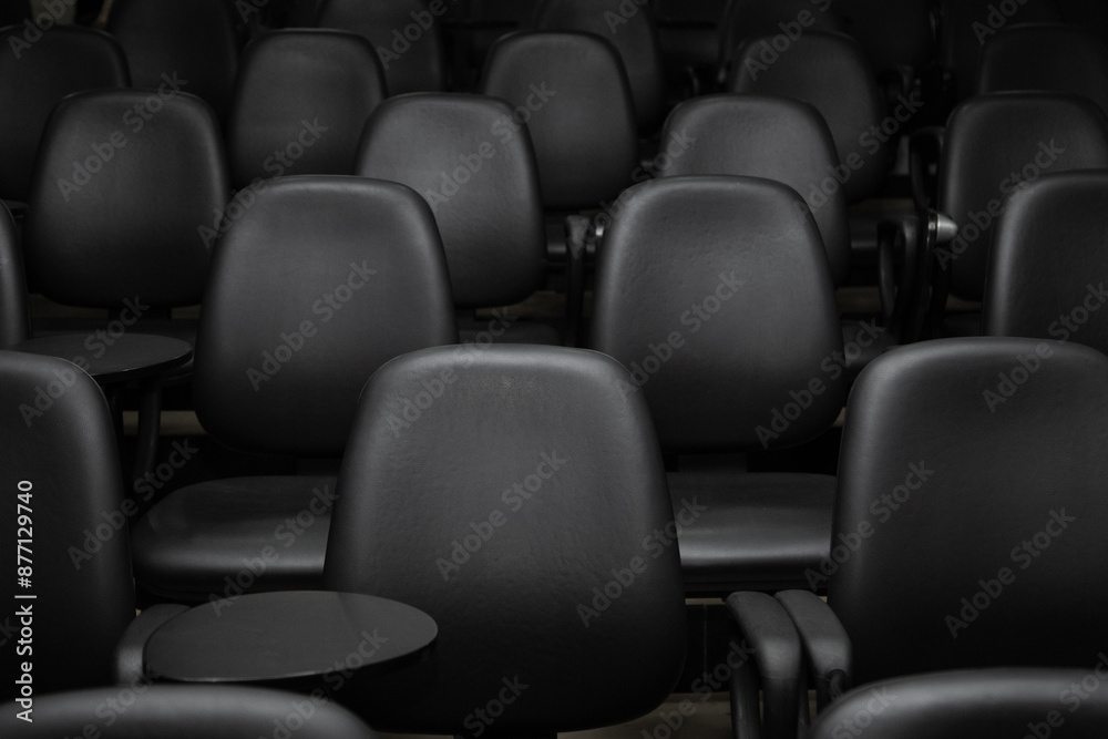 Close em algumas fileiras de poltronas pretas em um auditório vazio.