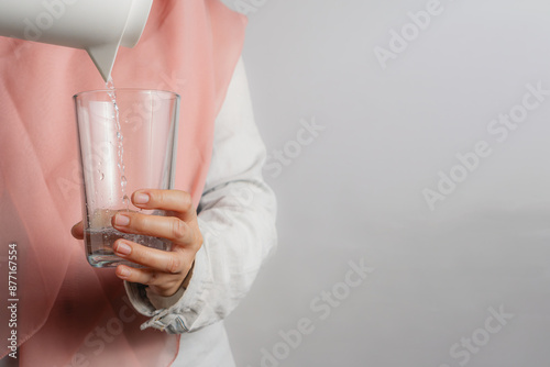 muslim woman with a peach color hijab or head scraft pouring water to a glass, concept of healthy lifestyle, gray background photo