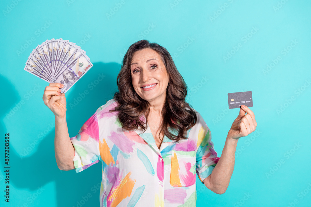 Photo portrait of lovely pensioner lady hold money fan credit card dressed stylish colorful garment isolated on cyan color background Photo portrait of lovely pensioner lady hold money fan credit card dressed stylish colorful garment isolated on cyan color background