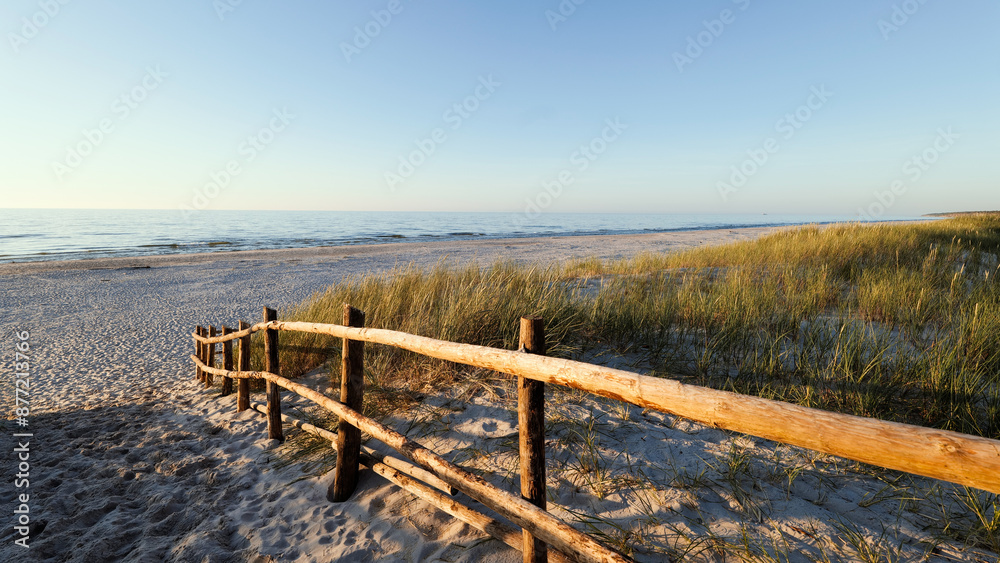 Beautiful wide beach on the Baltic Sea in the setting sun. Entrance to the beach. Wooden balustrade. Dunes covered with grass. Słaszczewo, Poland