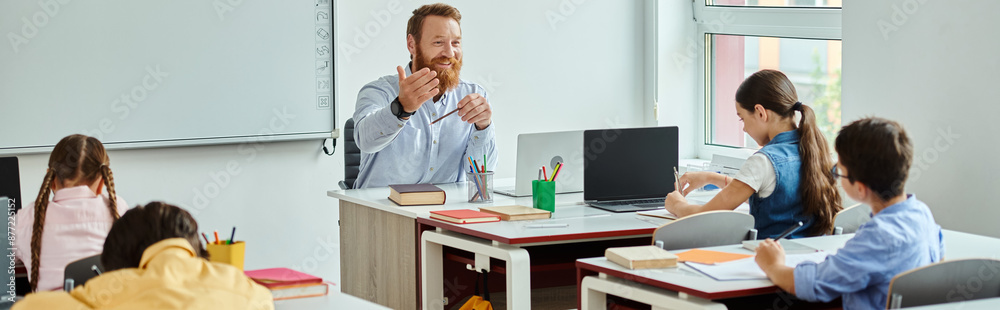 A man teacher stands confidently in front of a group of kids in a bright, lively classroom setting, actively instructing and engaging with the students. A man teacher stands confidently in front of a group of kids in a bright, lively classroom setting, actively instructing and engaging with the students.