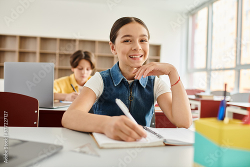 A young girl sits at a desk, deeply engrossed in her notebook