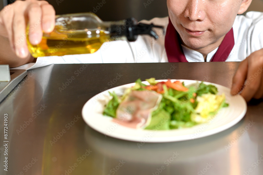 オリーブオイルをサラダにかける男性料理人