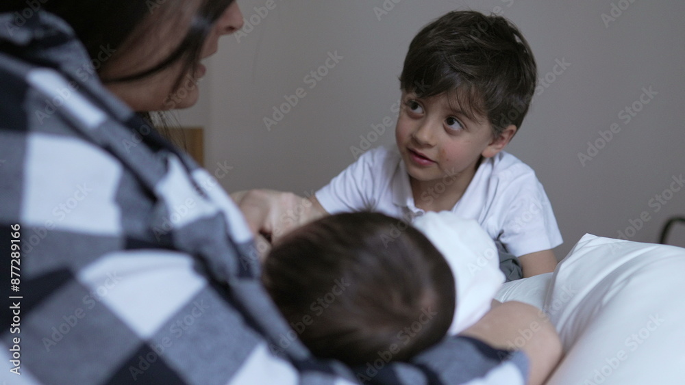 Obraz premium Young boy curiously watching his mother breastfeed his newborn sibling. mother wearing a plaid shirt, holds the baby lovingly while the boy looks on, capturing a moment of family bonding and curiosity