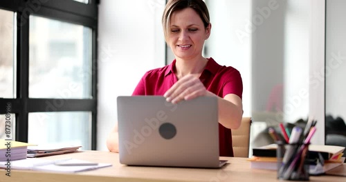Positive woman opens laptop to start working on project. Blonde female employee in red blouse sits at table ready to use device slow motion