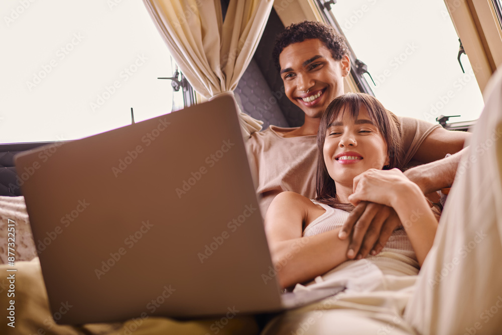 interracial couple sit on bed, engrossed in laptop screen in modern camper van interracial couple sit on bed, engrossed in laptop screen in modern camper van