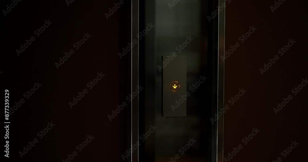 A close-up of the elevator call button, which glows yellow and shows a down arrow. Waiting for the elevator to go down to the floor below. A close-up of the elevator call button, which glows yellow and shows a down arrow. Waiting for the elevator to go down to the floor below.