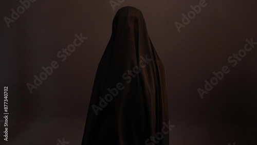 a mystical priestess under a black veil, a woman in black on a dark background, the wind sways the fabric on her face