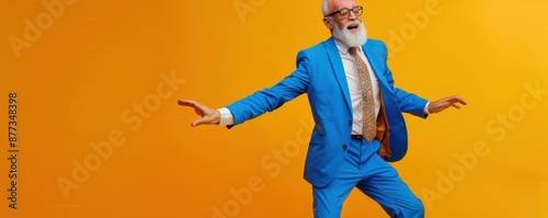 Obraz na płótnie Elderly man in a blue suit dancing against a vibrant orange background. Free copy space for banner. w salonie