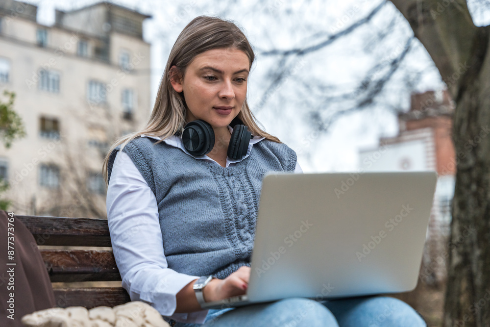 Young business woman graphic designer professional working on laptop computer sitting on park bench. Introvert businessperson work alone outside of the crowded office building for better concentration Young business woman graphic designer professional working on laptop computer sitting on park bench. Introvert businessperson work alone outside of the crowded office building for better concentration
