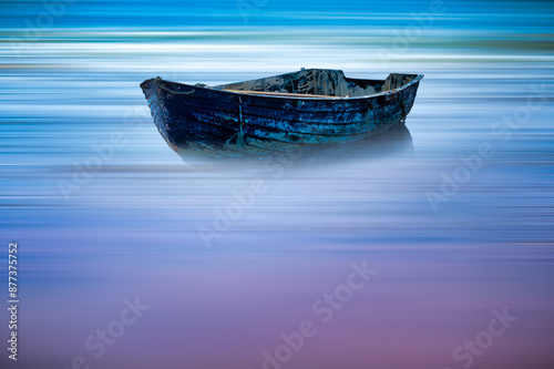 A solitary old boat floats on calm, misty waters with a vibrant, blurred backdrop of blues and purples.