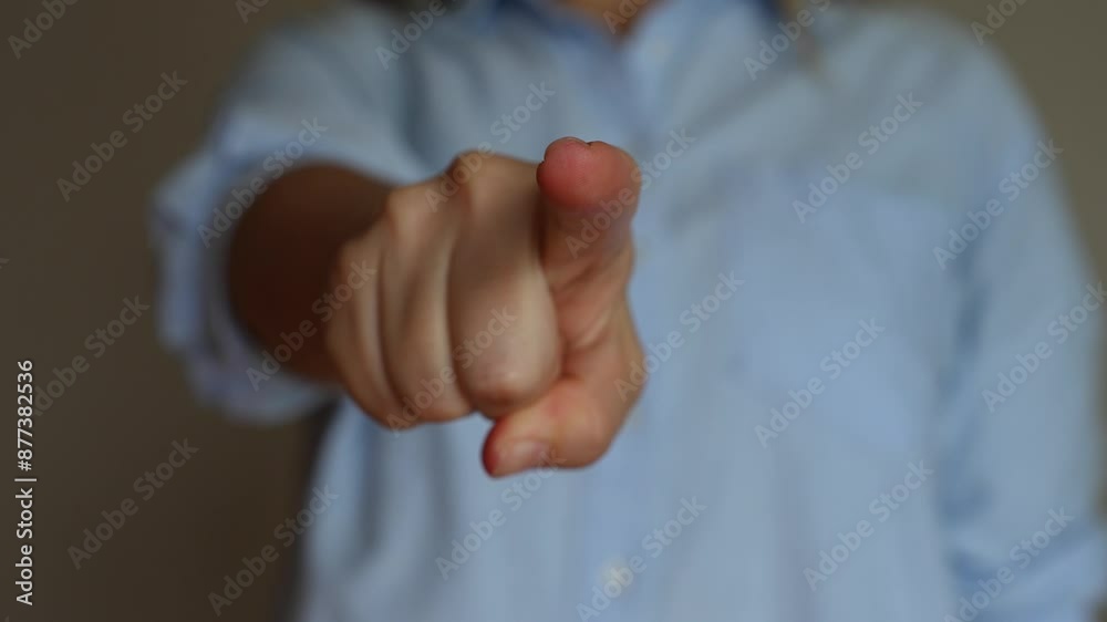 Cropped shot of a young woman in a blue shirt pointing forward into the screen with her hand on a beige background. Pointing finger gesture. The sign that means I choose you. Changing focus