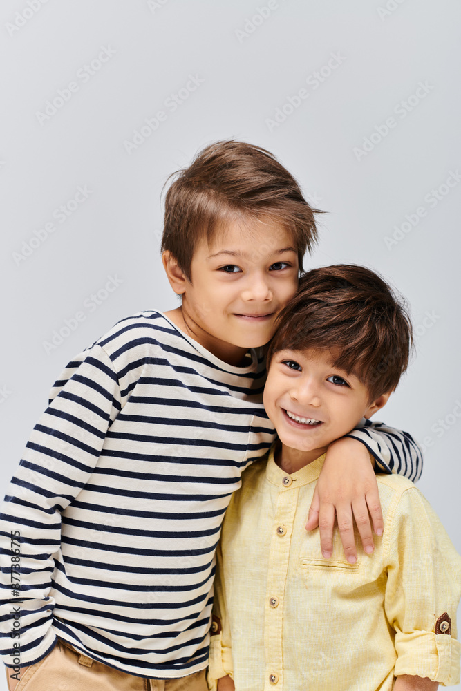 Two young boys, one standing confidently and the other with a playful smile, pose for a portrait in a studio setting. Two young boys, one standing confidently and the other with a playful smile, pose for a portrait in a studio setting.