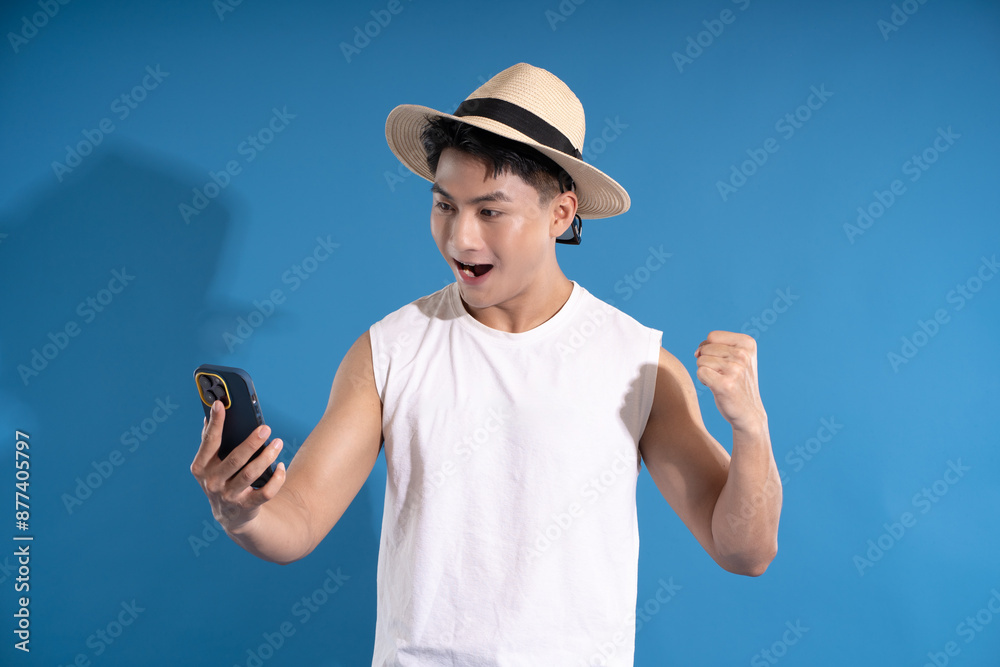 Portrait of asian guy wearing summer outfit using phone and posing on blue background Portrait of asian guy wearing summer outfit using phone and posing on blue background
