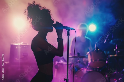 A female vocalist performs on stage, bathed in purple and blue light, her silhouette illuminated against a backdrop of hazy stage lights photo