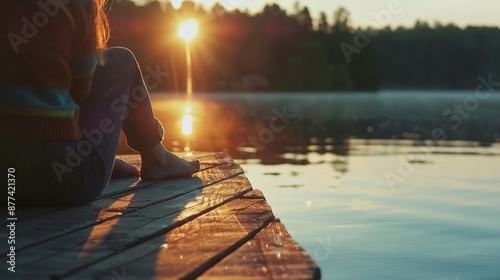 A women sits on the edge of a dock, feet dangling over the water, watching the sunrise. The camera is close, focusing on the back of the women, capturing the moment of peace and introspection photo