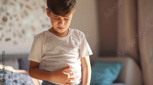 Concerned boy holding his stomach, indicating discomfort, with a pained expression in a home setting photo