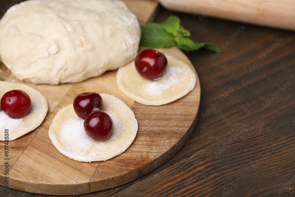Process of making dumplings (varenyky) with cherries. Raw dough and ingredients on wooden table, closeup Process of making dumplings (varenyky) with cherries. Raw dough and ingredients on wooden table, closeup