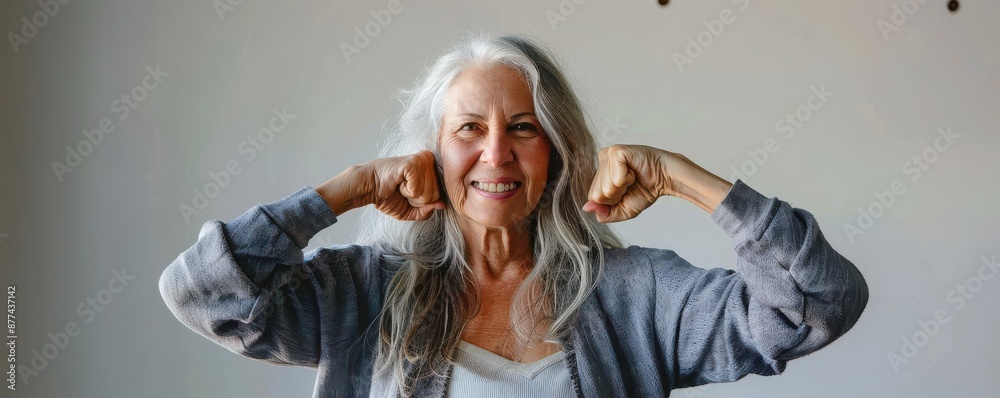 Happy senior woman flexing muscles and smiling, showing strength and confidence. Free copy space.