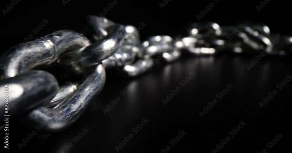 Long iron chain leaves reflection on dark table surface. Shiny chain links designed for bijouterie. Steel equipment on black background macro