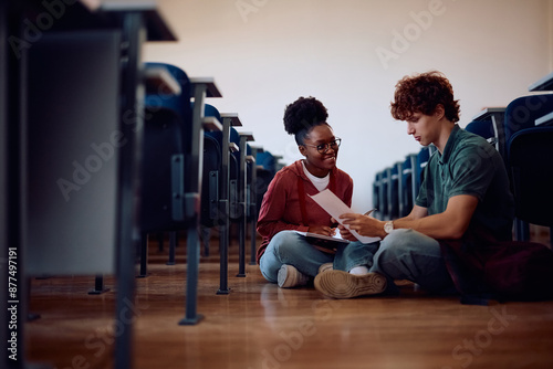 Happy college friends learning together while sitting on floor in classroom.