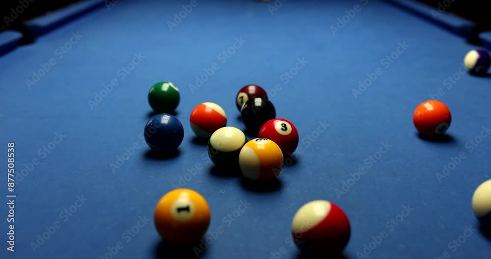 Focused player with cue aims at pyramid of colorful balls with digits. Man enjoys playing billiard on blue pool table in club slow motion