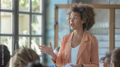 A confident woman passionately speaks in a classroom setting, engaging her audience with expressive hand gestures and a focused demeanor. photo