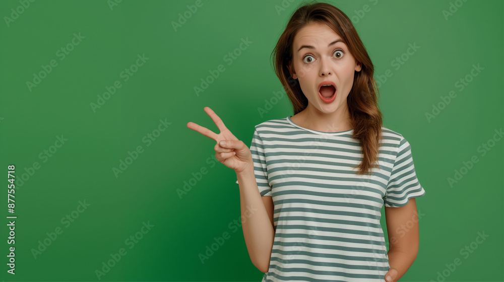 Woman in a green striped shirt making a surprised face with a peace sign, captured against a solid green background. Woman in a green striped shirt making a surprised face with a peace sign, captured against a solid green background.