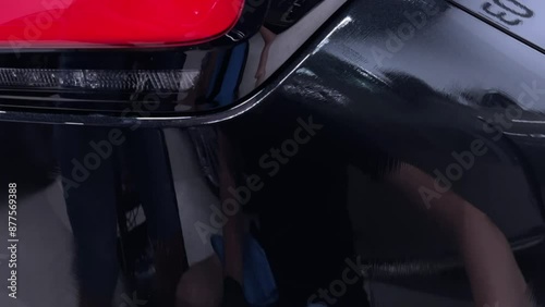 Car detailing studio employee applies a ceramic coating, starting by pouring the coating onto an applicator. The video highlights the meticulous process and attention to detail