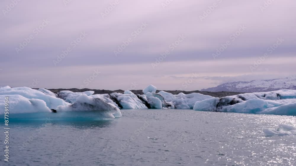 Blue and white icebergs float in a glacial lake against a backdrop of glaciers, creating a serene scene. Unspoiled Jokulsarlon, Iceland. Blue and white icebergs float in a glacial lake against a backdrop of glaciers, creating a serene scene. Unspoiled Jokulsarlon, Iceland.