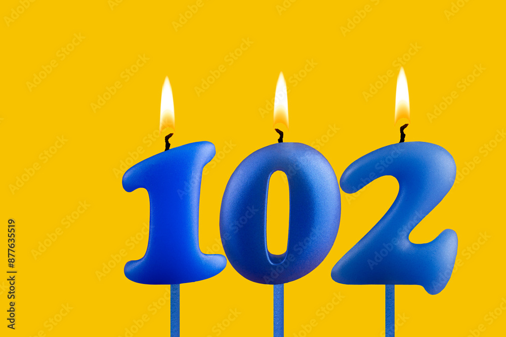 Blue birthday candle on yellow background - Number 102 Blue birthday candle on yellow background - Number 102